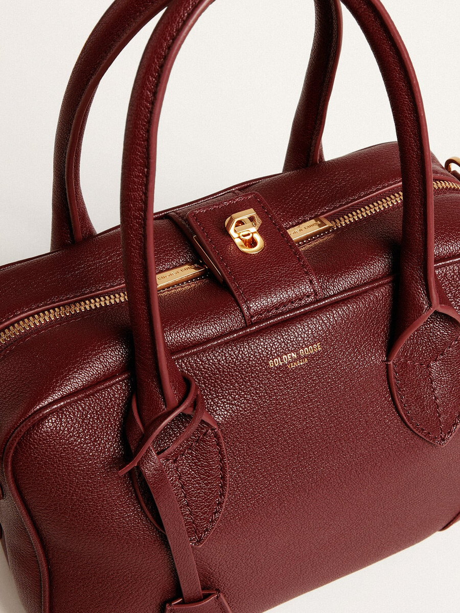 vita-tasche aus burgunderrotem leder mit goldenen details